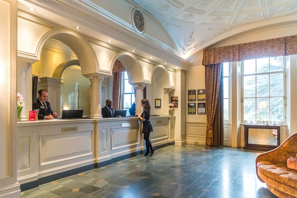 Macdonald Bath Spa Hotel Εσωτερικό φωτογραφία The photo shows the interior of a hotel reception area. There is a stylish front desk with several staff members attending to guests. A woman is interacting with one of the receptionists. The design features elegant architectural details, including a