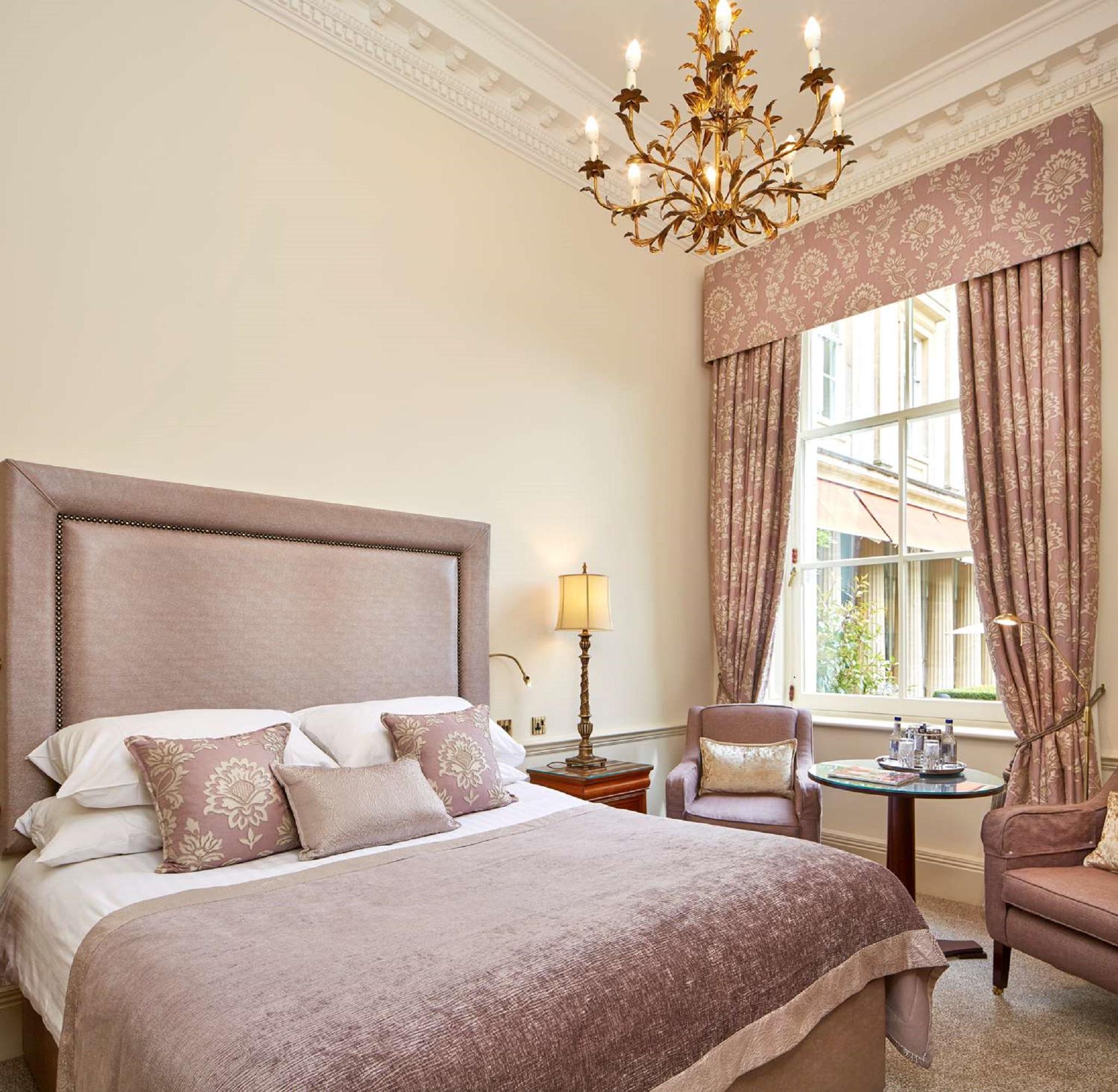 Macdonald Bath Spa Hotel Εξωτερικό φωτογραφία The photo shows a beautifully decorated hotel room. It features a large bed with a plush headboard, adorned with several decorative pillows. The walls are painted in a soft color, and there is a chandelier hanging from the ceiling. Natural light come