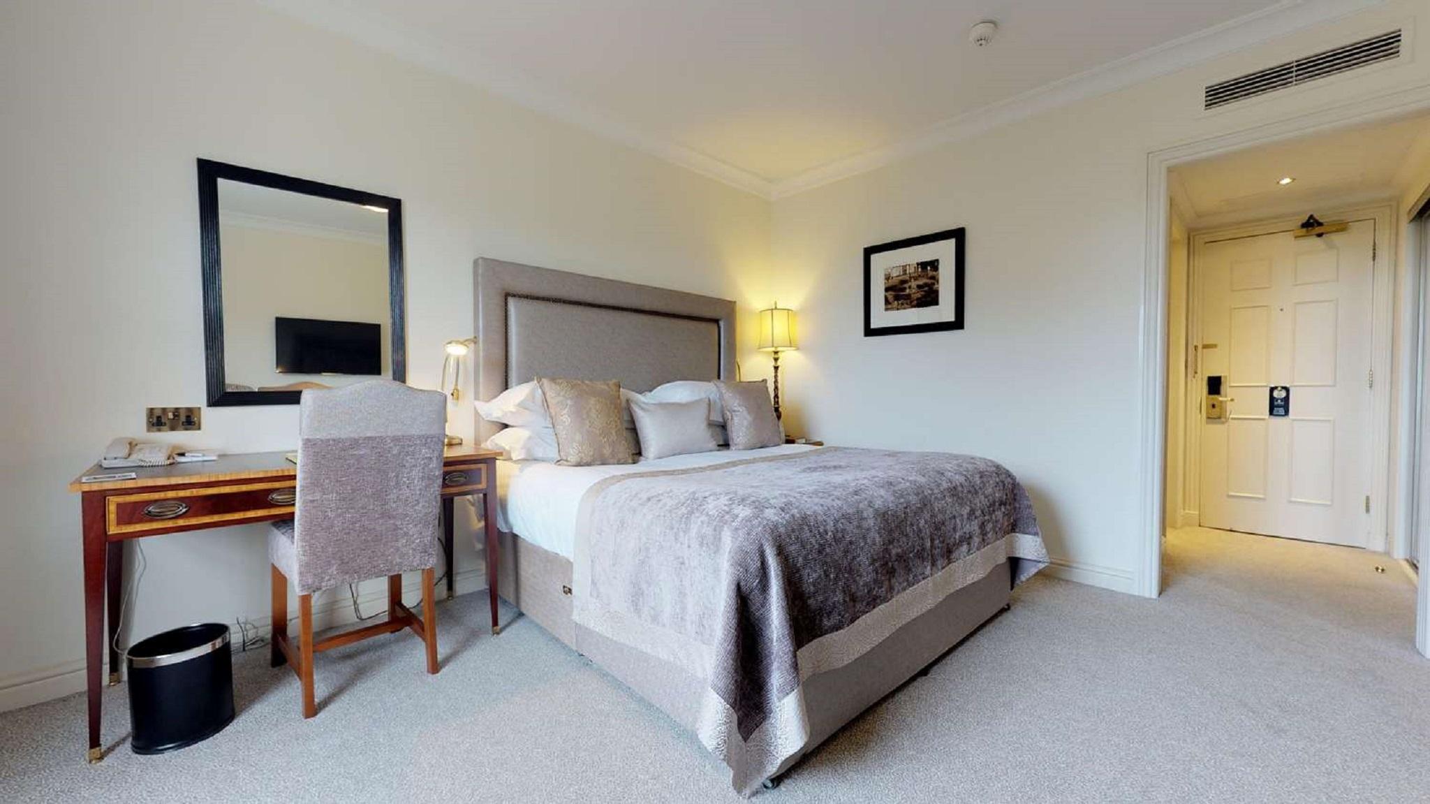 Macdonald Bath Spa Hotel Εξωτερικό φωτογραφία The photo shows a well-decorated hotel room. In the center, there's a comfortable bed with plush bedding and decorative pillows. A bedside table with a lamp is positioned next to the bed. To the left, there's a small desk with a chair, accompanied by