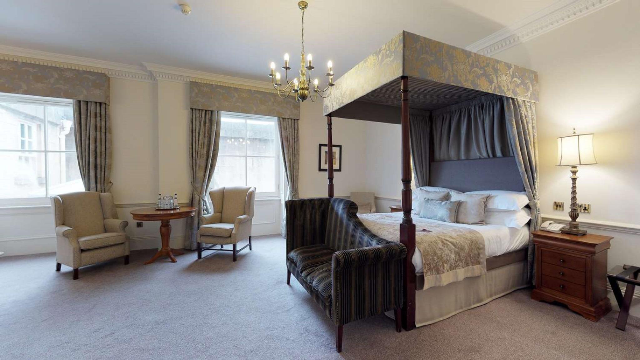 Macdonald Bath Spa Hotel Εξωτερικό φωτογραφία The photo shows a stylish hotel room featuring a four-poster bed with a decorative canopy. The bed is positioned prominently in the center, surrounded by plush bedding. To the side, there are two armchairs with a small round table between them, creat