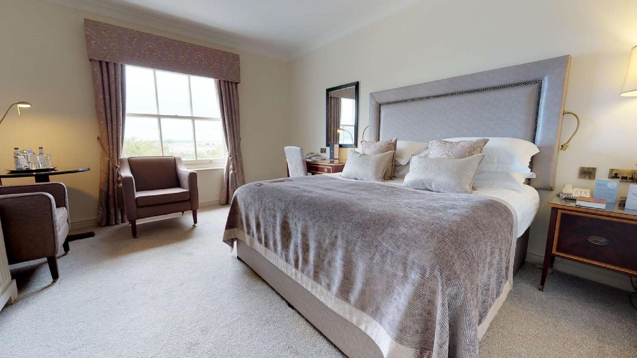 Macdonald Bath Spa Hotel Εξωτερικό φωτογραφία The photo shows a well-furnished bedroom. It features a large bed with a light gray headboard and several decorative pillows on top. The bed is covered with a soft gray blanket. To one side of the room, there is a comfortable armchair and a small tab