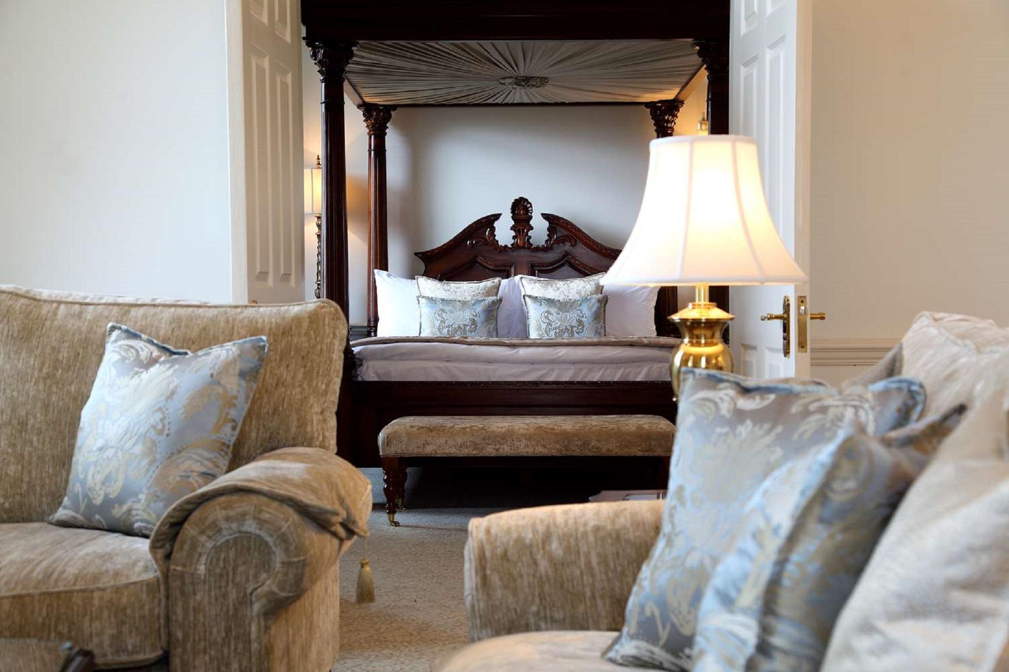 Macdonald Bath Spa Hotel Εξωτερικό φωτογραφία The photo shows a beautifully decorated room featuring a four-poster bed in the background. The bed has a wooden frame with a rich design, and it is adorned with plush bedding and pillows. In the foreground, there are comfortable sofas with decorativ