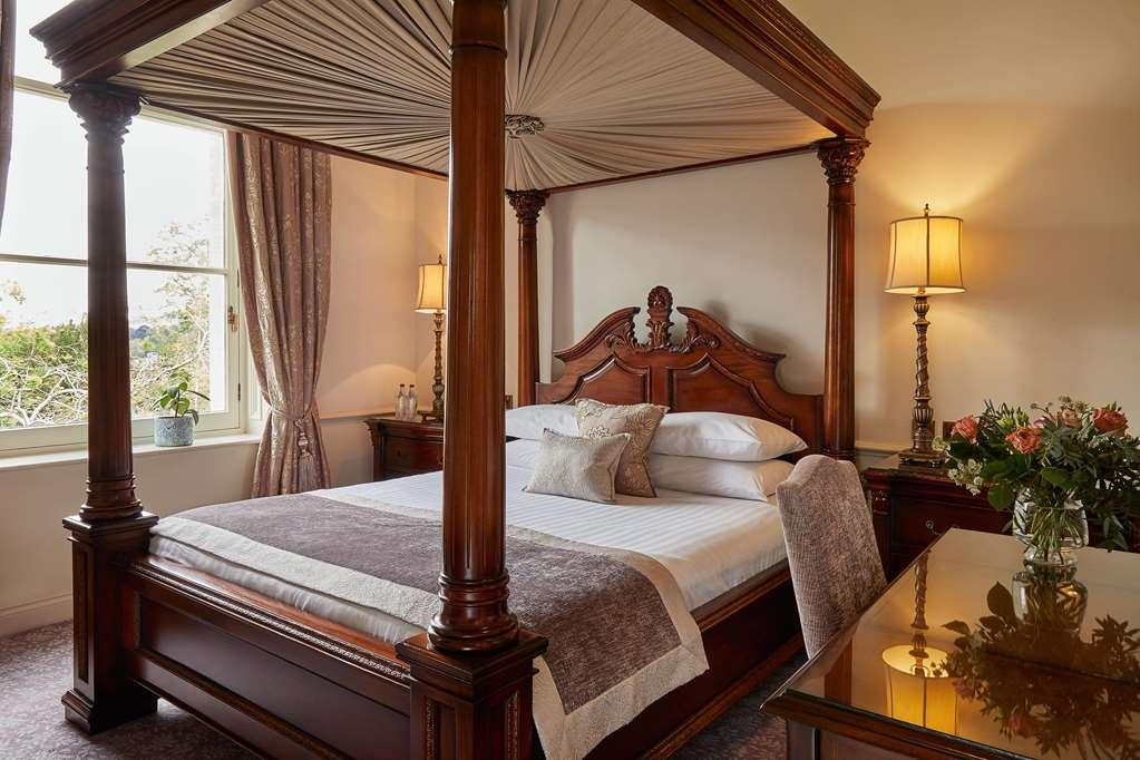 Macdonald Bath Spa Hotel Δωμάτιο φωτογραφία The photo shows a beautifully designed bedroom featuring a four-poster bed made of dark wood. The bed has an elaborately carved headboard and is adorned with a light-colored bedding set. Above the bed, there is a canopy that adds an elegant touch. On