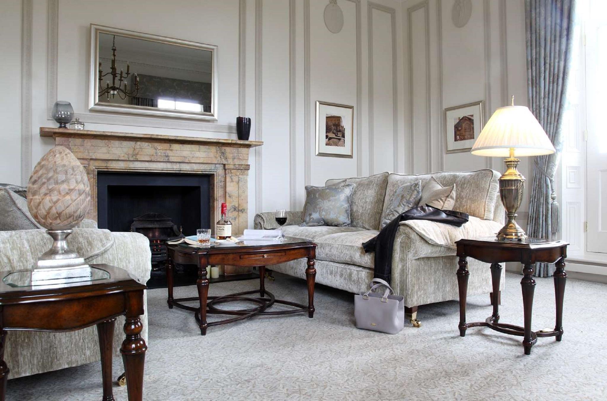 Macdonald Bath Spa Hotel Εξωτερικό φωτογραφία The photo shows a stylish living room. It features a plush light-colored sofa adorned with decorative pillows. Next to the sofa, there is a small wooden coffee table with a decorative item and a bottle of wine, along with a glass. A larger wooden tab