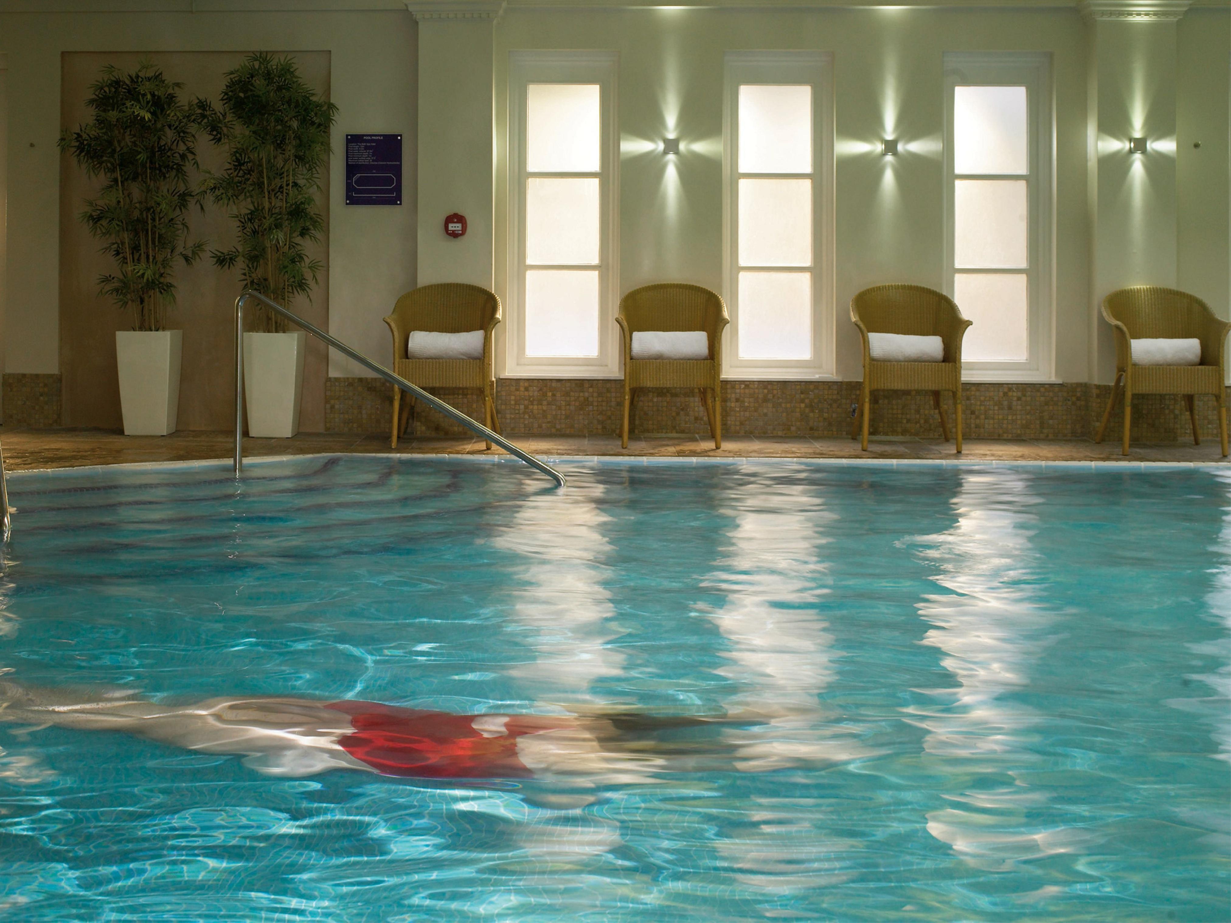 Macdonald Bath Spa Hotel Εξωτερικό φωτογραφία The photo shows an indoor swimming pool with clear, blue water. In the pool, a person is swimming, partially submerged, and wearing a red swimsuit. Surrounding the pool, there are several empty chairs arranged along the side, along with potted plants