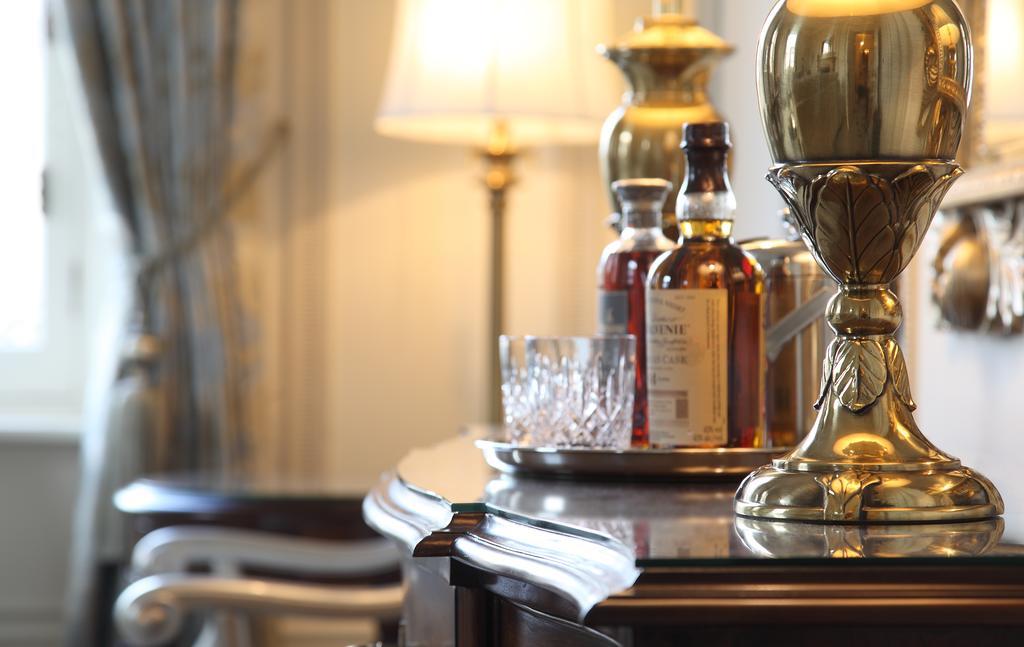Macdonald Bath Spa Hotel Εξωτερικό φωτογραφία The photo features an elegant interior scene that includes a polished wooden bar or table. On the surface, there are several bottles of liquor, likely whiskey, each with a distinctive label. A glass, possibly for drinking, is positioned near the bott